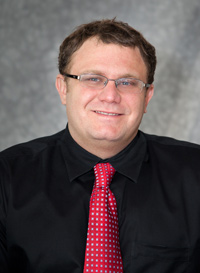 Dr. Cottingham wearing a black shirt and red tie (headshot). 